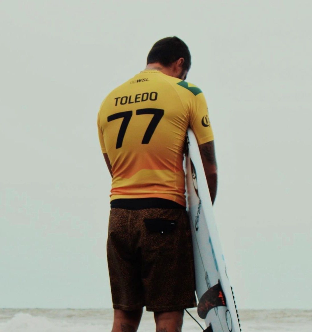 Filipe Toledo praying on the beach, holding his surfboard