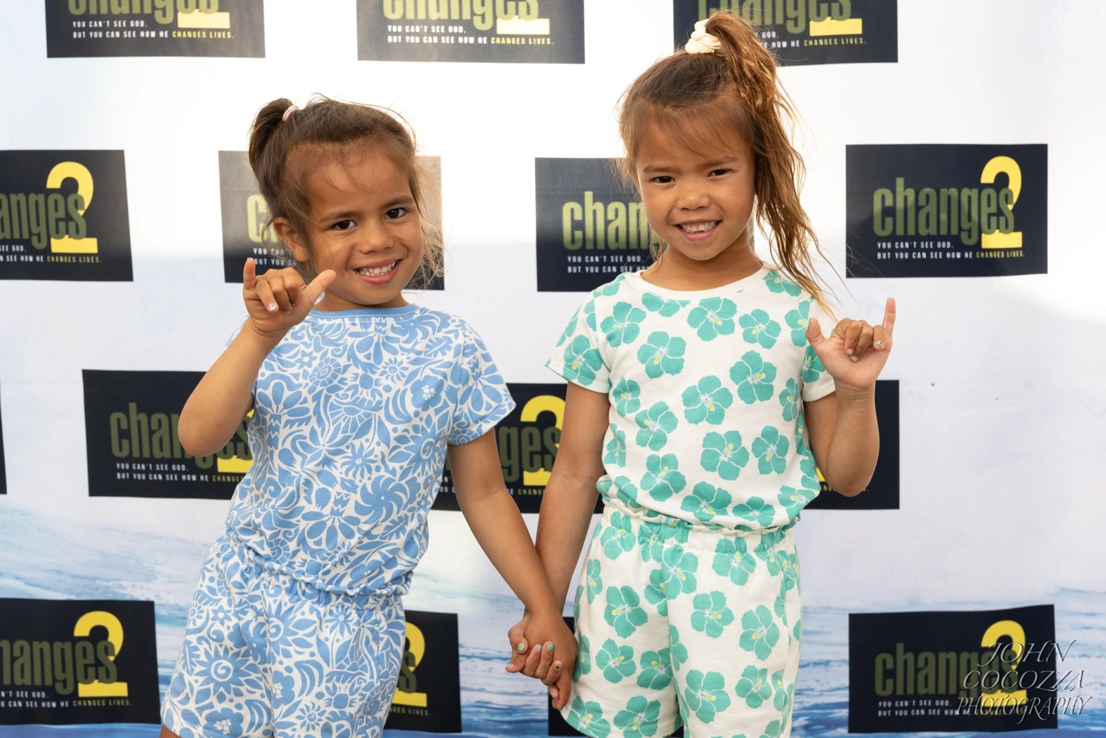 Two young girls throwing shakas at the premiere backdrop